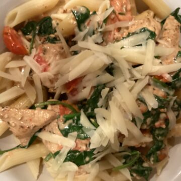 creamy tuscan chicken with penne pasta placed on a white plate