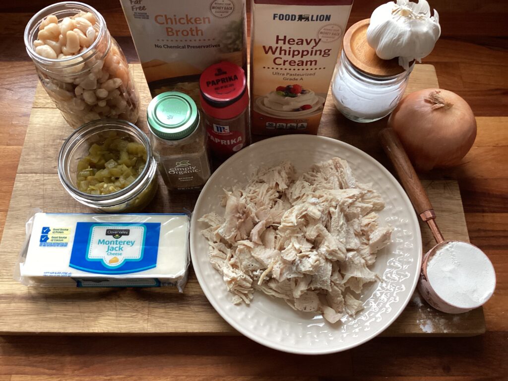 A wooden cutting board filled with ingredients for making white chicken chili.